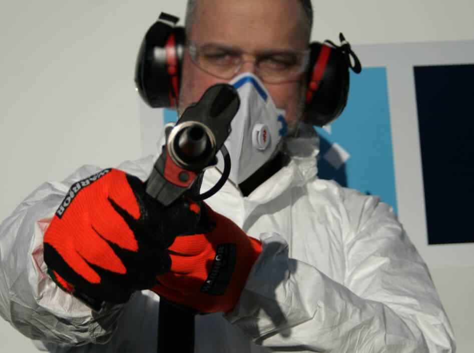 Man in overalls and PPE holding a dry ice blaster with the nozzle facing the camera.